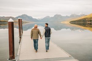 Two people walk hand in hand on wooden dock with misty mountain lake reflecting morning light.