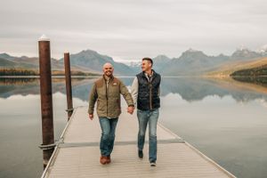 Two people walking together on a wooden dock over a serene mountain lake with reflective waters.