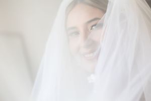 Soft ethereal portrait of a bride wearing a white veil smiling through the delicate tulle fabric.