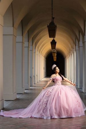 An elegant pink ballgown with a flowing train photographed in a dramatic arched hallway with hanging lanterns.
