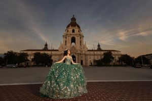 A person in a sparkling emerald green ballgown poses in front of Pasadena City Hall during sunset.