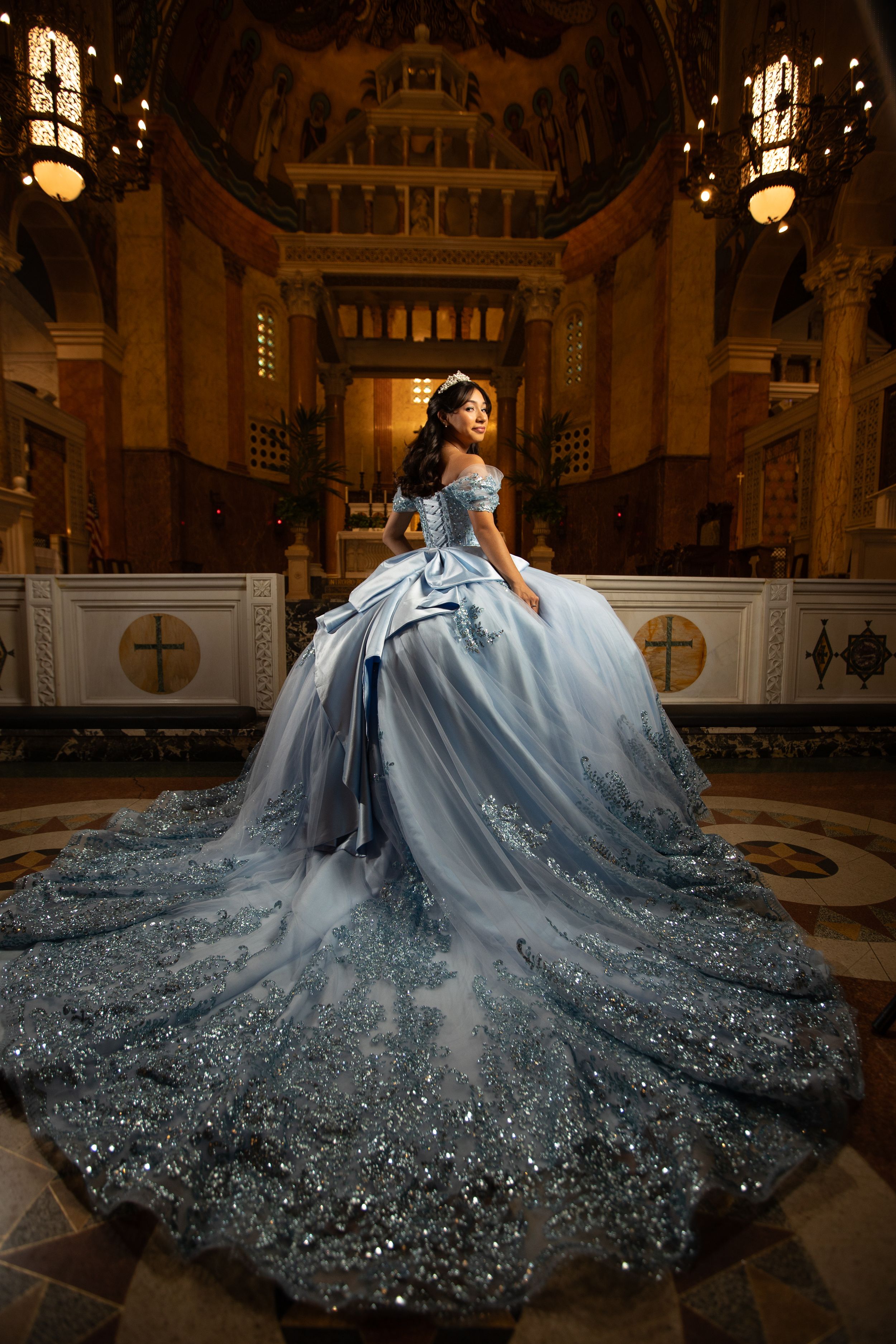 A dramatic light blue ballgown with sparkling details and a sweeping cathedral-length train photographed in an ornate church setting.