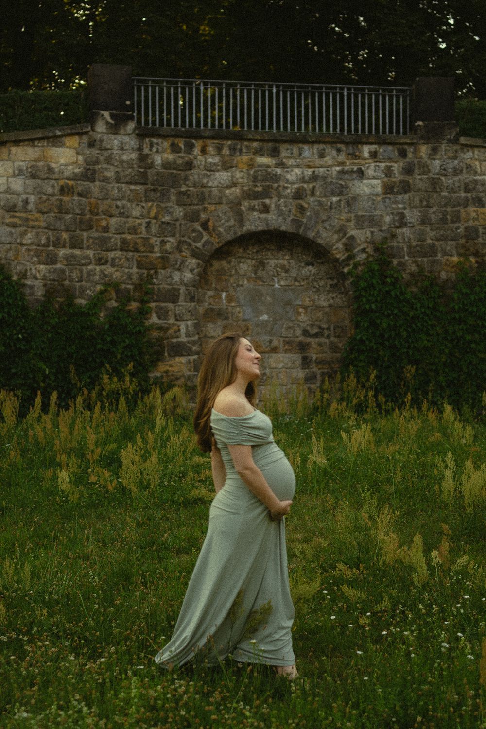 Babybauchfotoshooting - Lächelnde Frau im Kleid hält schwangeren Bauch und spaziert durch den Palaisgarten im Japanischen Palais Dresden