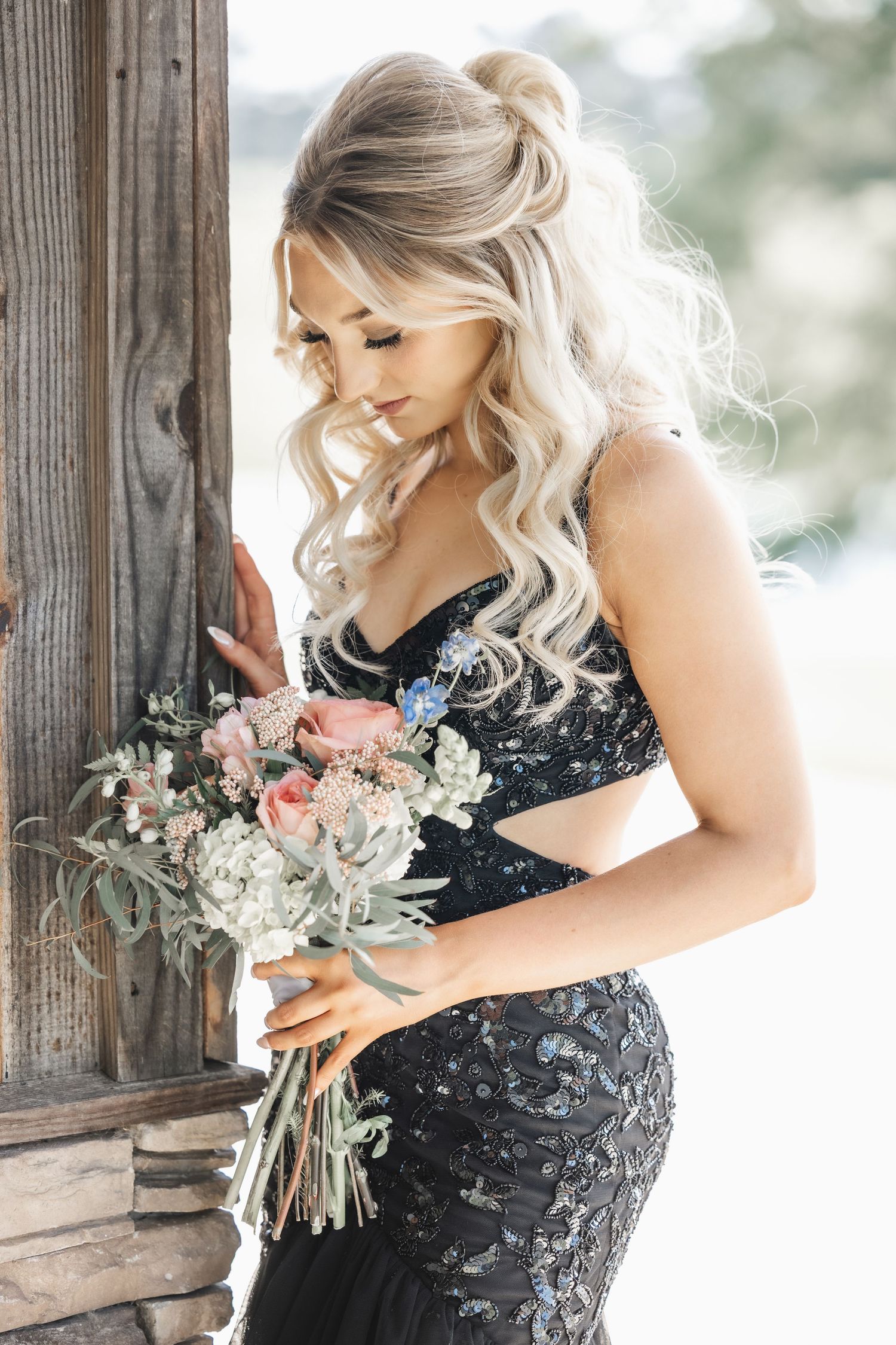 Elegant woman in black dress holding floral bouquet against rustic wooden backdrop.