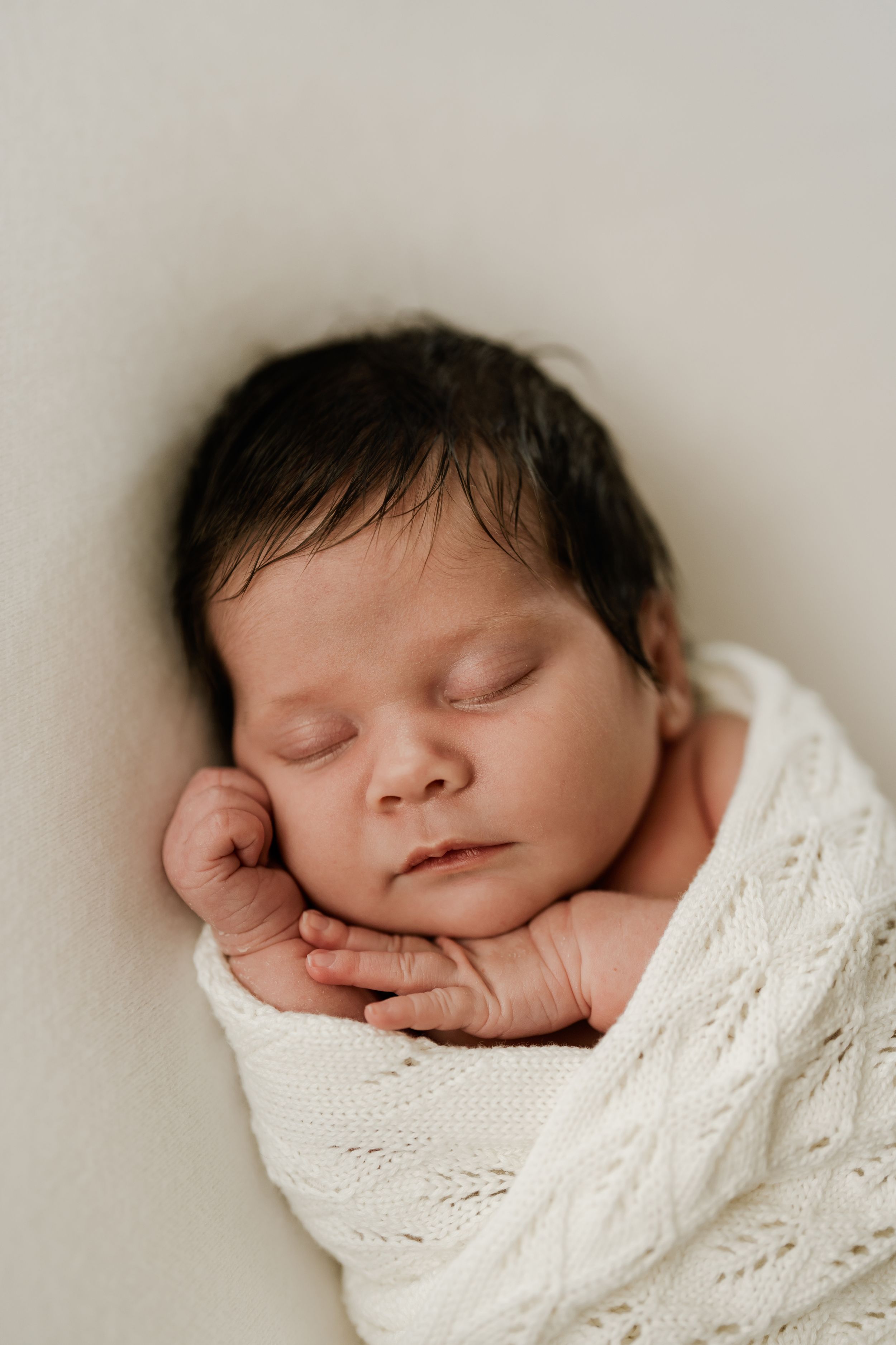 Sleeping peaceful newborn wrapped in a white blanket during an in-home newborn photography session