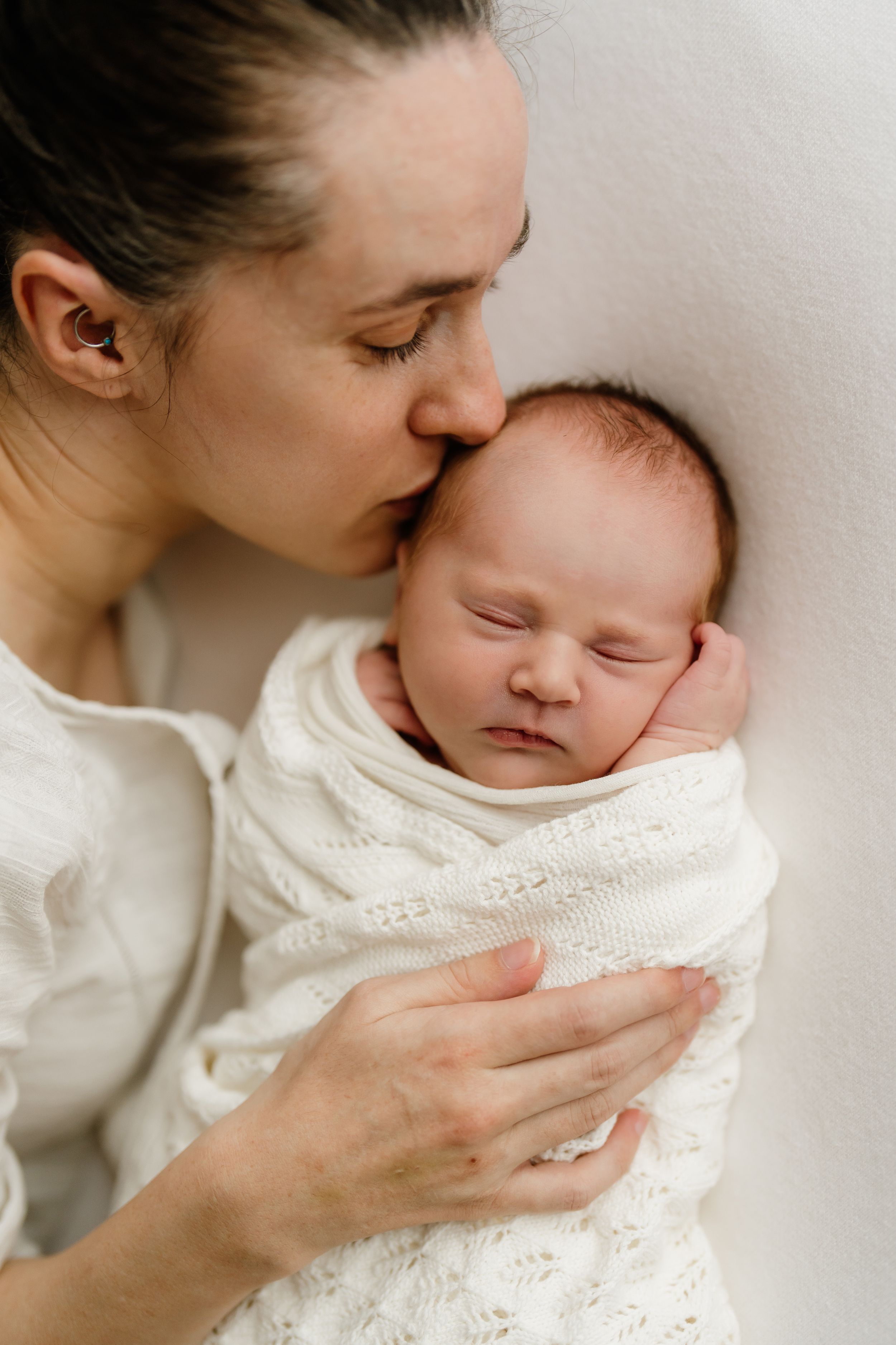 Intimate newborn photography – mother kissing sleeping baby in natural light