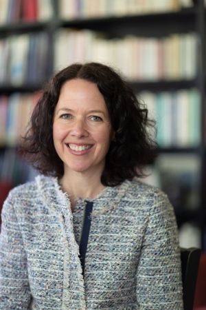 A professional portrait in front of a bookshelf wearing a tweed jacket.