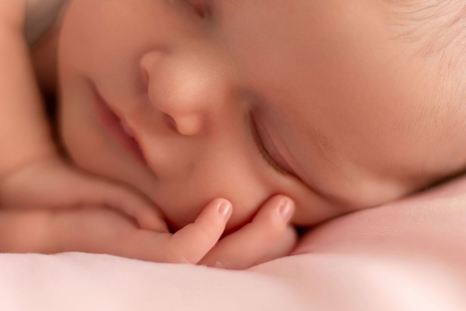 Close-up view of a sleeping newborn with soft peachy skin tones in natural lighting.