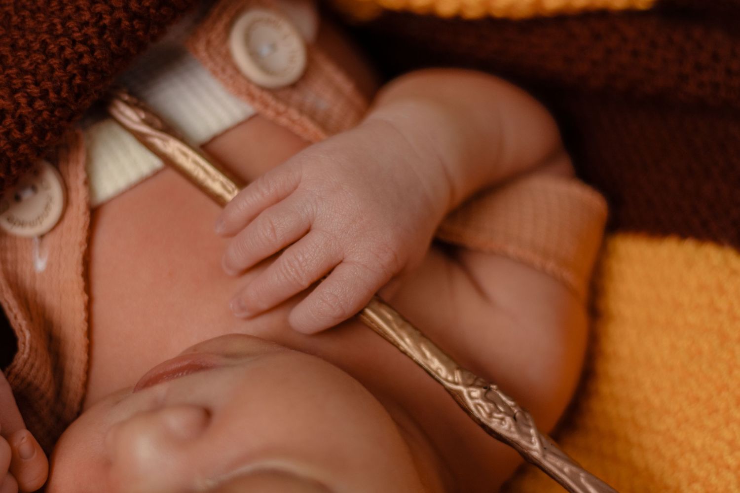 Sleeping baby wearing brown knit hat resting on orange blanket.