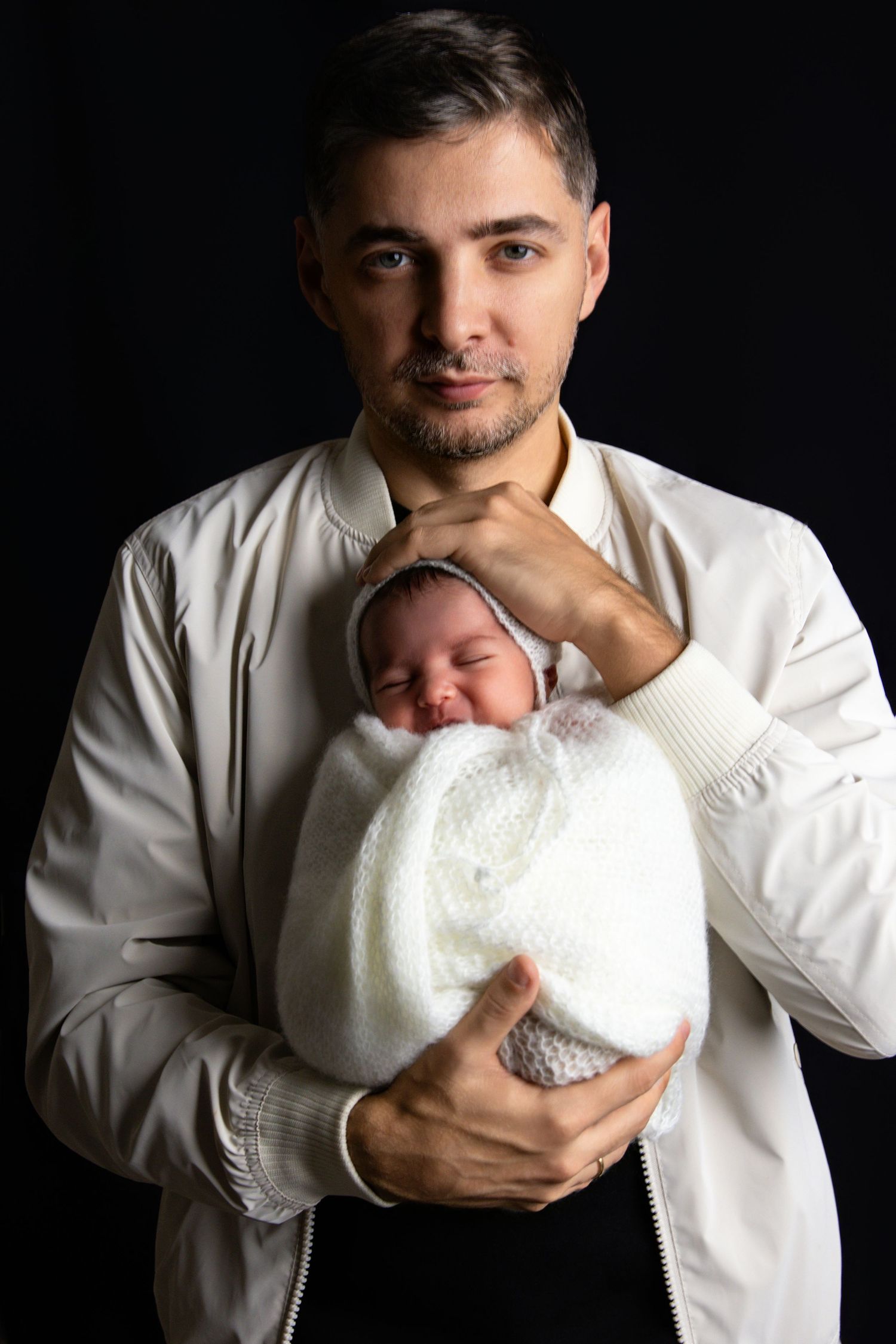 A series of intimate black and white portraits showing a person in white holding a swaddled newborn baby.