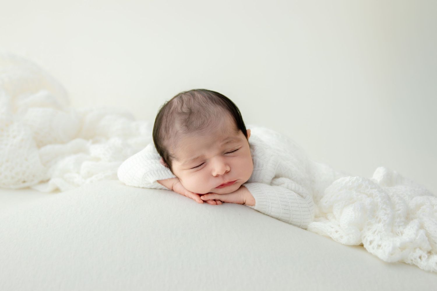 Peaceful sleeping newborn baby rests on white blanket with lace trim during professional photo session.