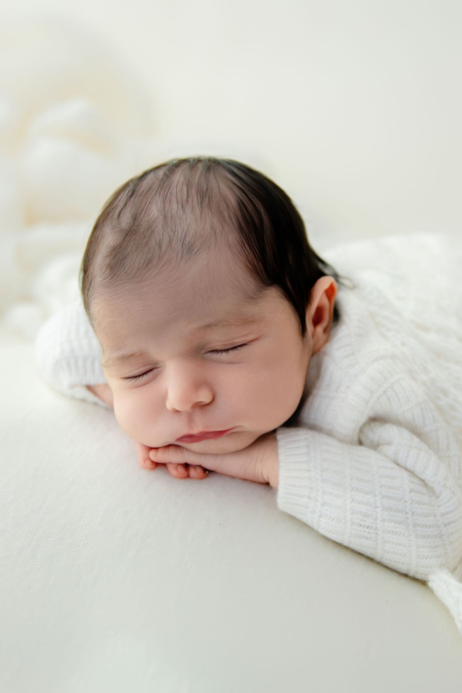 Peaceful sleeping newborn baby in white sweater resting on soft white blanket.