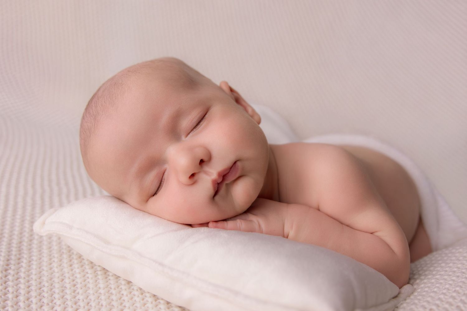 Peaceful sleeping newborn baby resting on soft white textured blanket in gentle lighting.