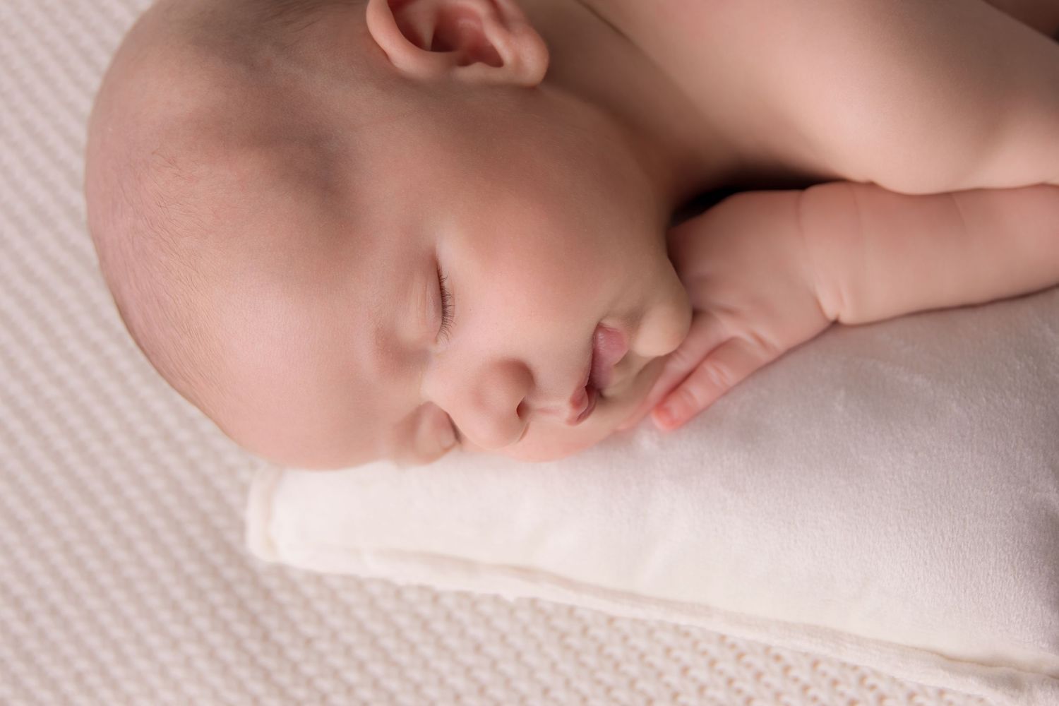 A peaceful sleeping baby rests on a soft white pillow with tiny hand curled near their face.