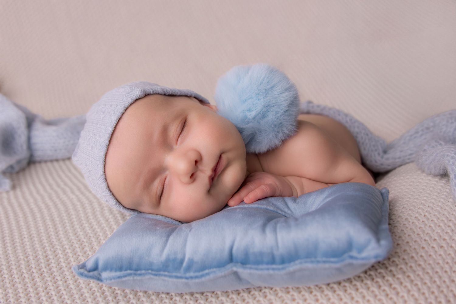Peaceful sleeping baby wrapped in soft blue blanket lying on textured white bedding.
