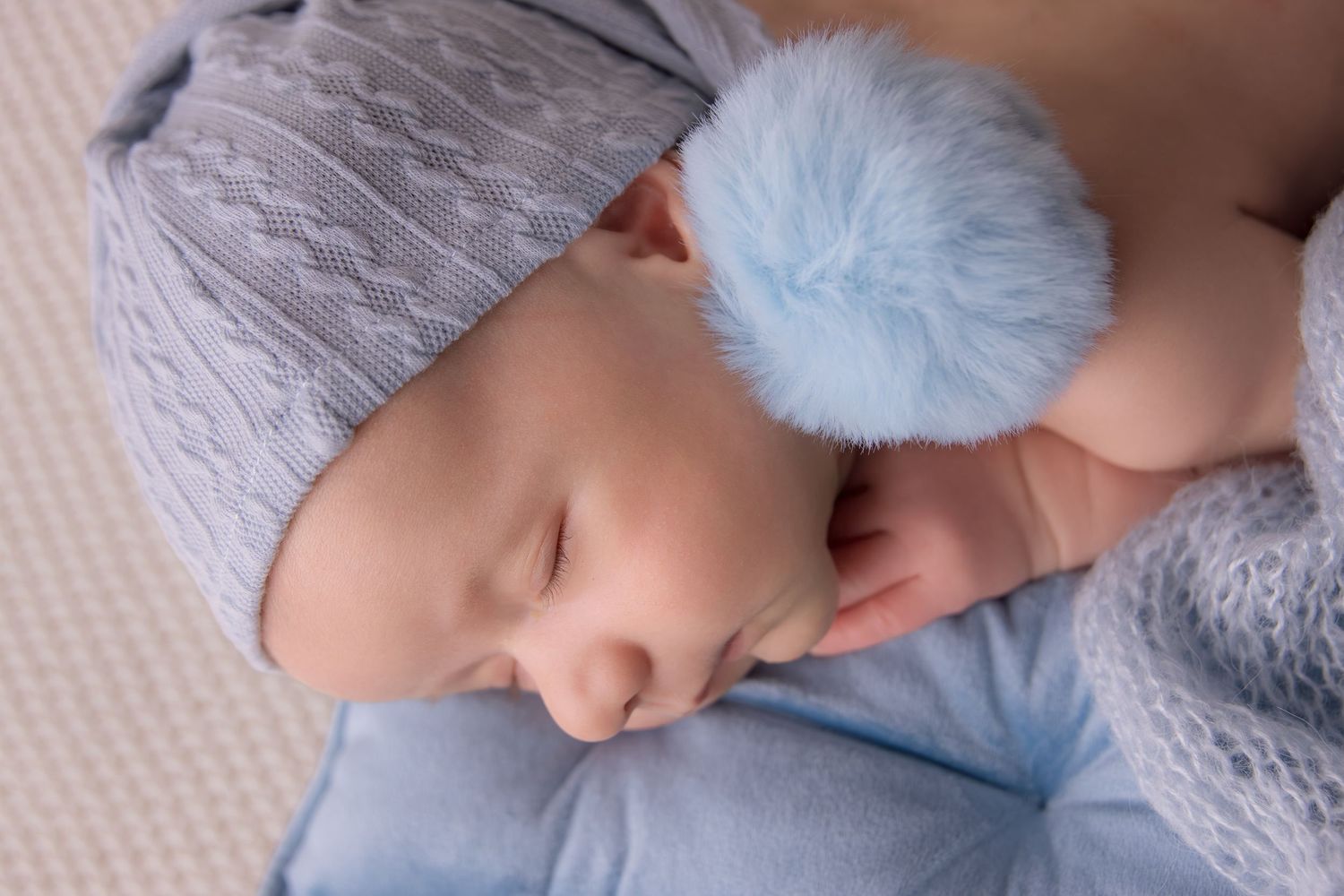 A sleeping baby in a blue hat rests peacefully on a soft gray blanket.