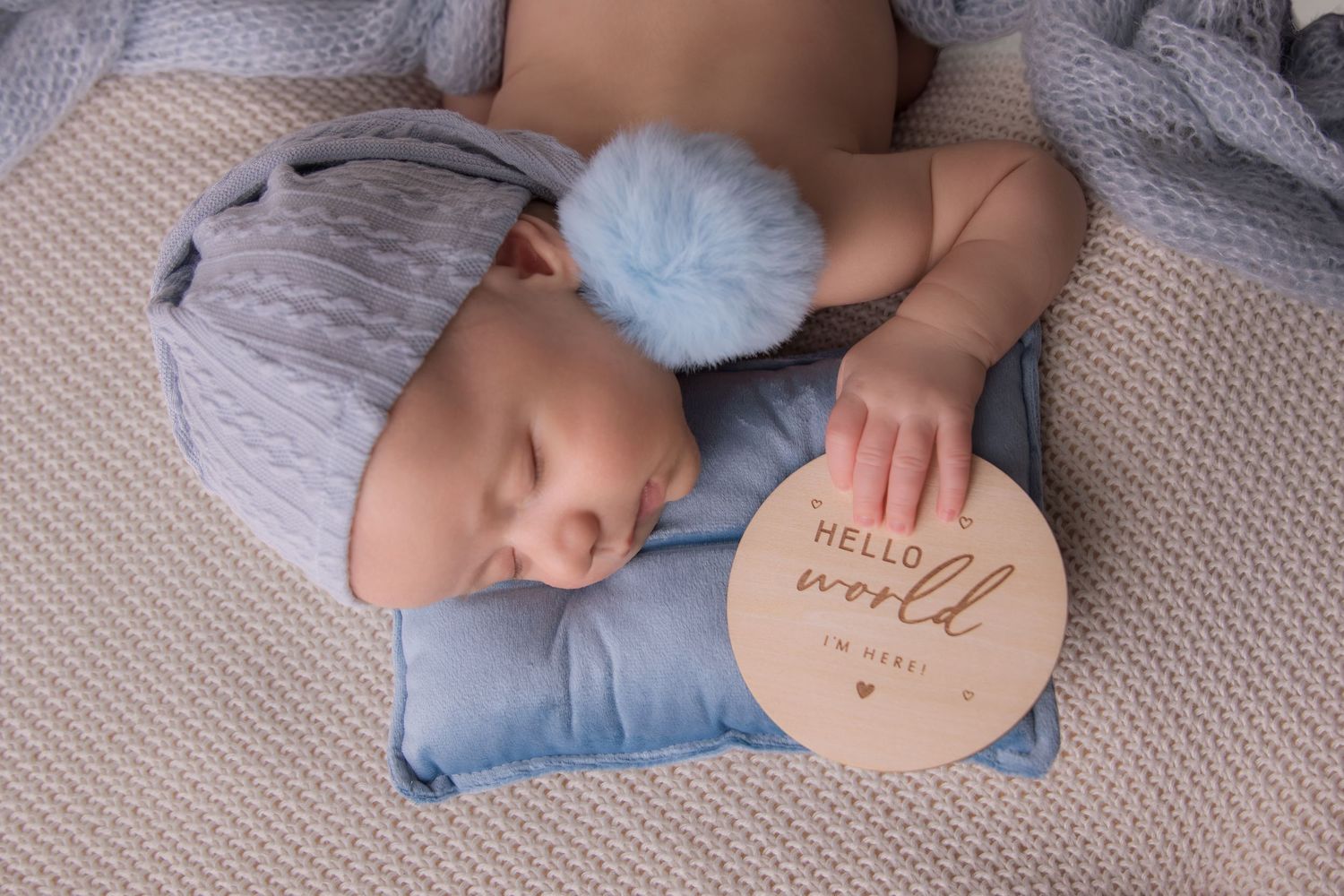 Newborn baby lying on soft blanket with heart-shaped wooden sign displaying birth announcement details.