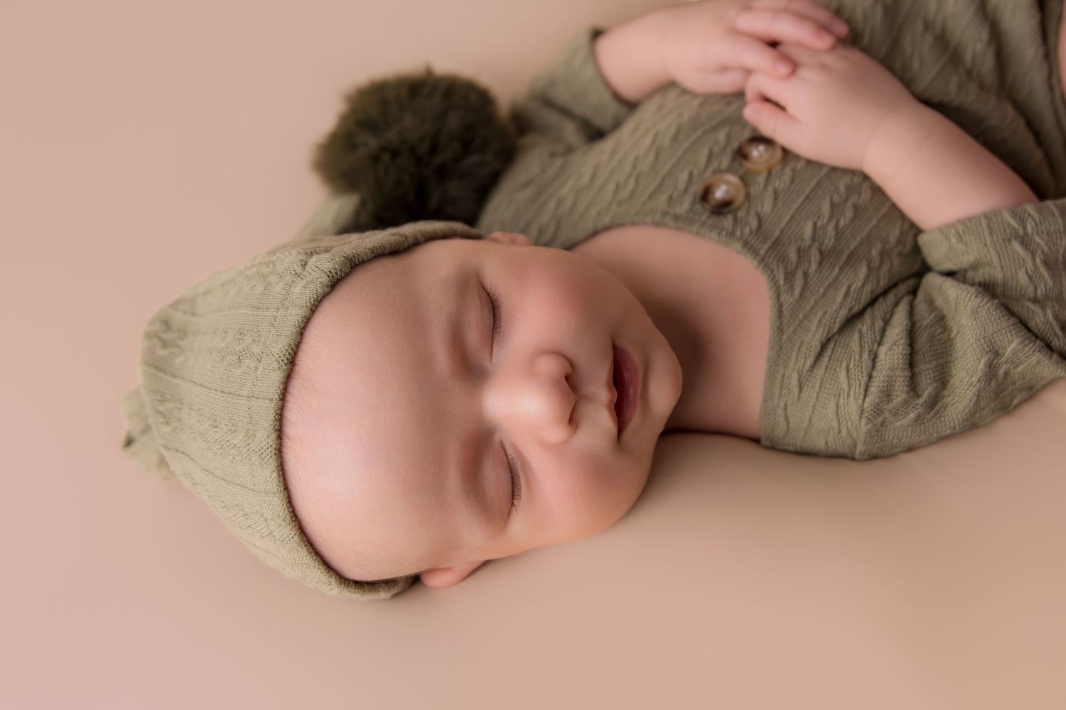Sleeping baby in neutral beige clothing lies peacefully on soft textured fabric.