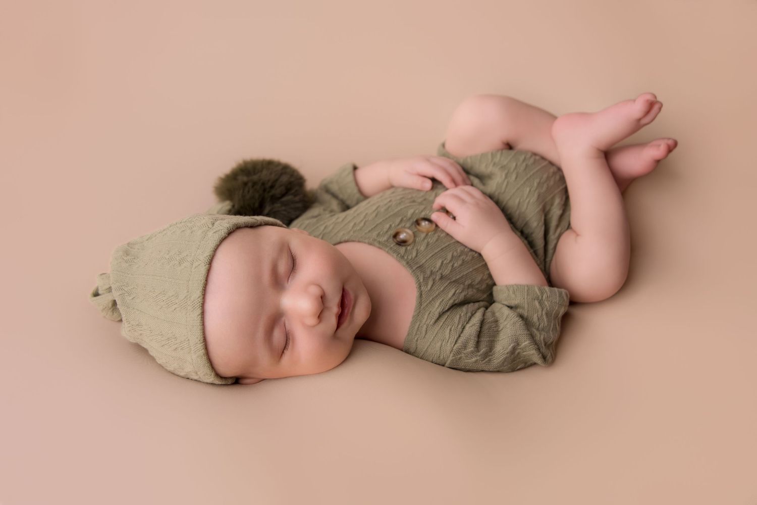 Sleeping newborn baby in soft pink and beige tones lies peacefully on textured blanket in professional studio setting.