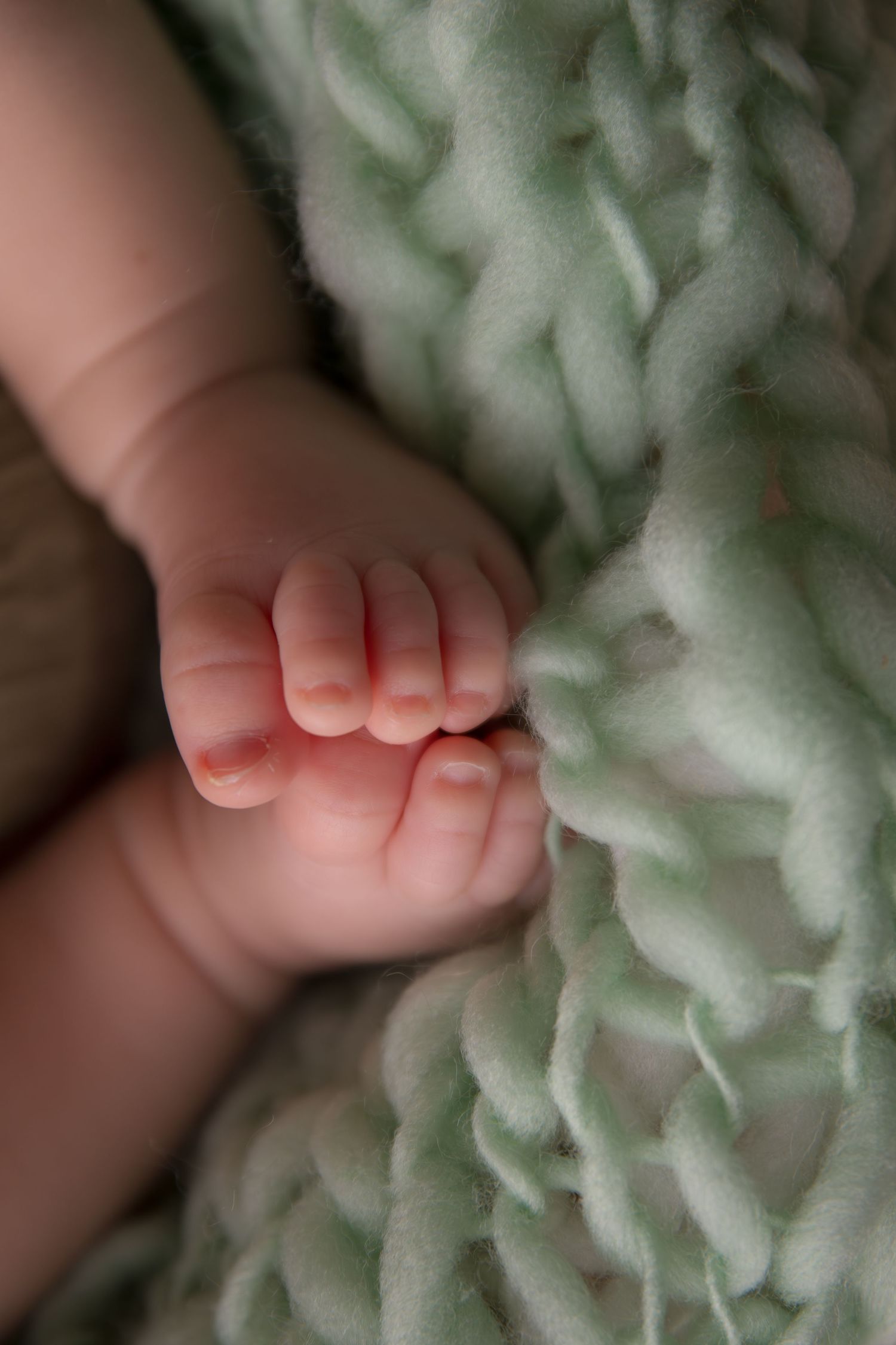 Close-up photo of tiny baby toes resting on soft mint green textured fabric.