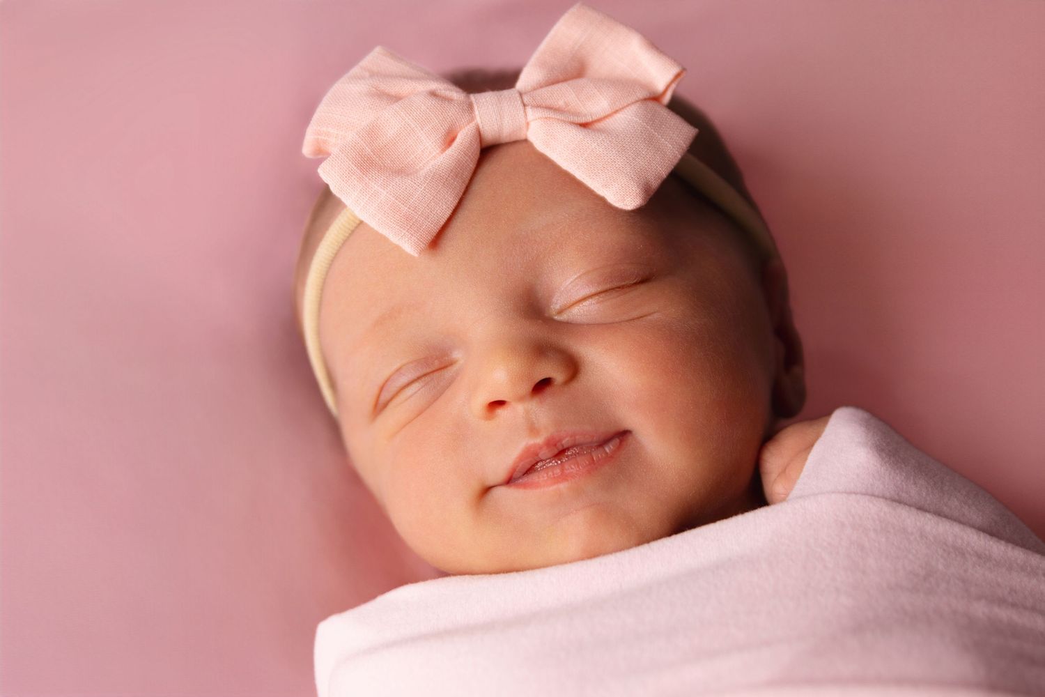 Sleeping newborn baby in soft pink lighting during professional photo session.
