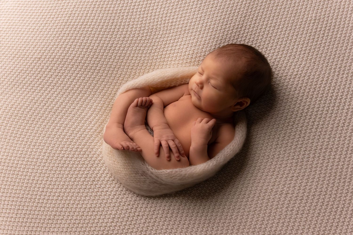 Sleeping newborn posed on textured beige background.