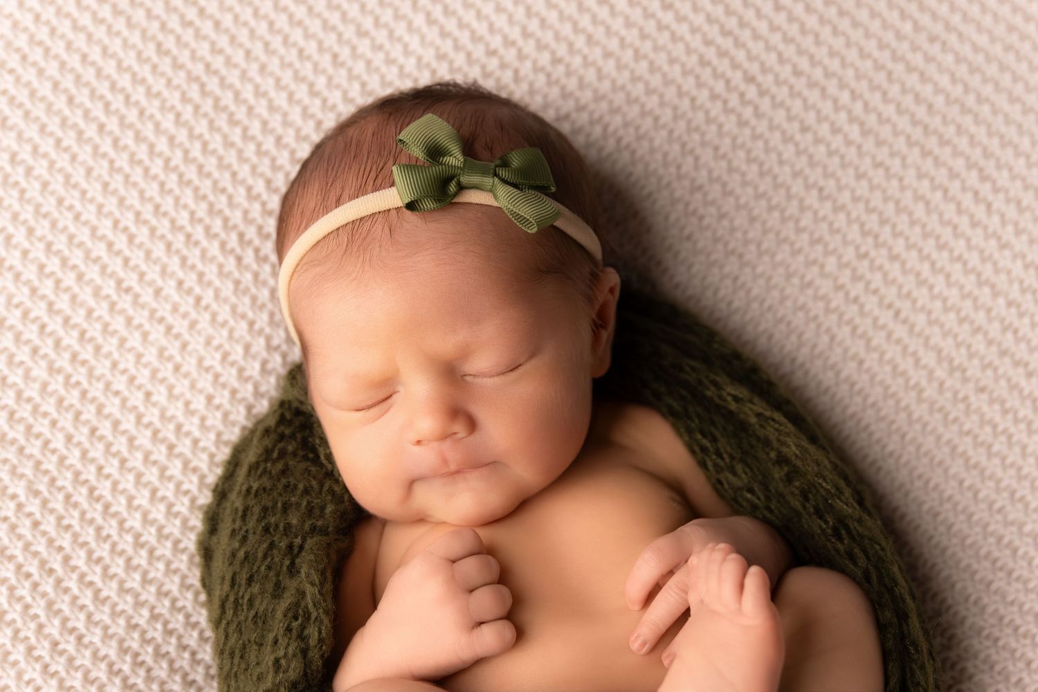 Newborn baby sleeping on textured backdrop with green headband.