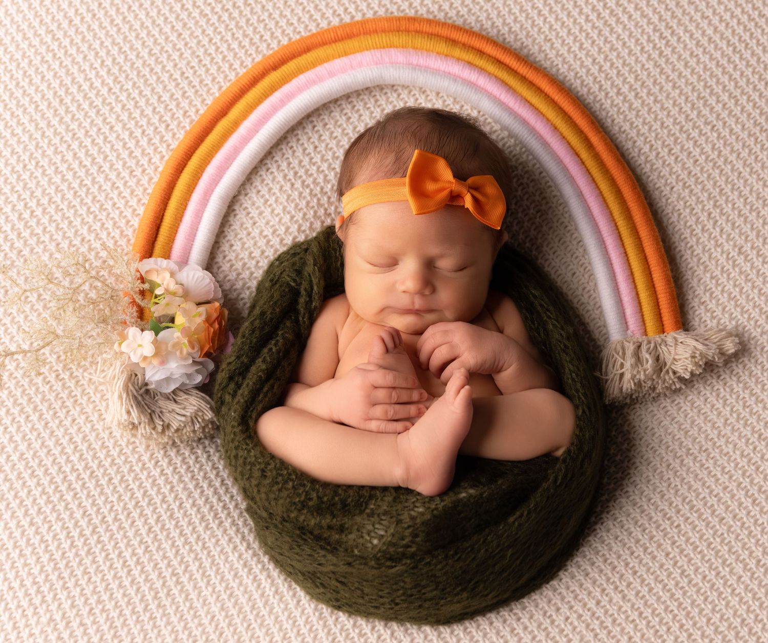 Artistic newborn photo series with rainbow arch decorations on cream textured background.