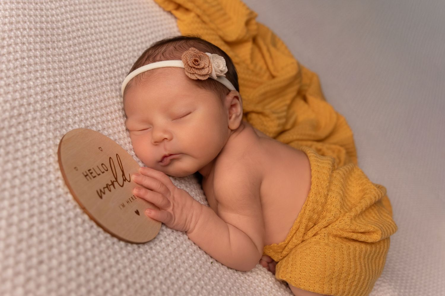 Newborn photography session with mustard yellow wrap and wooden props on neutral background.