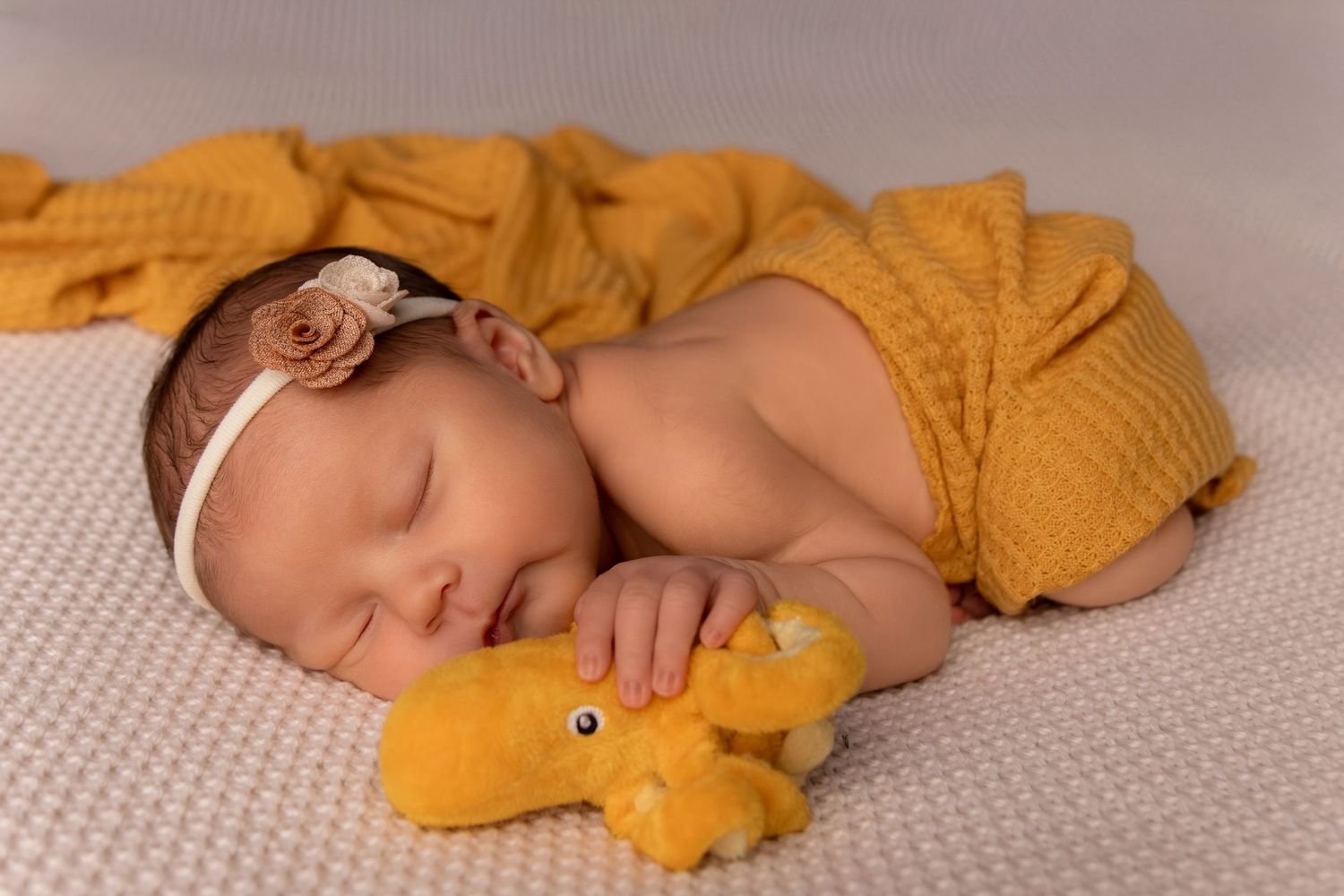 Sweet newborn portrait with mustard yellow accessories and soft lighting.