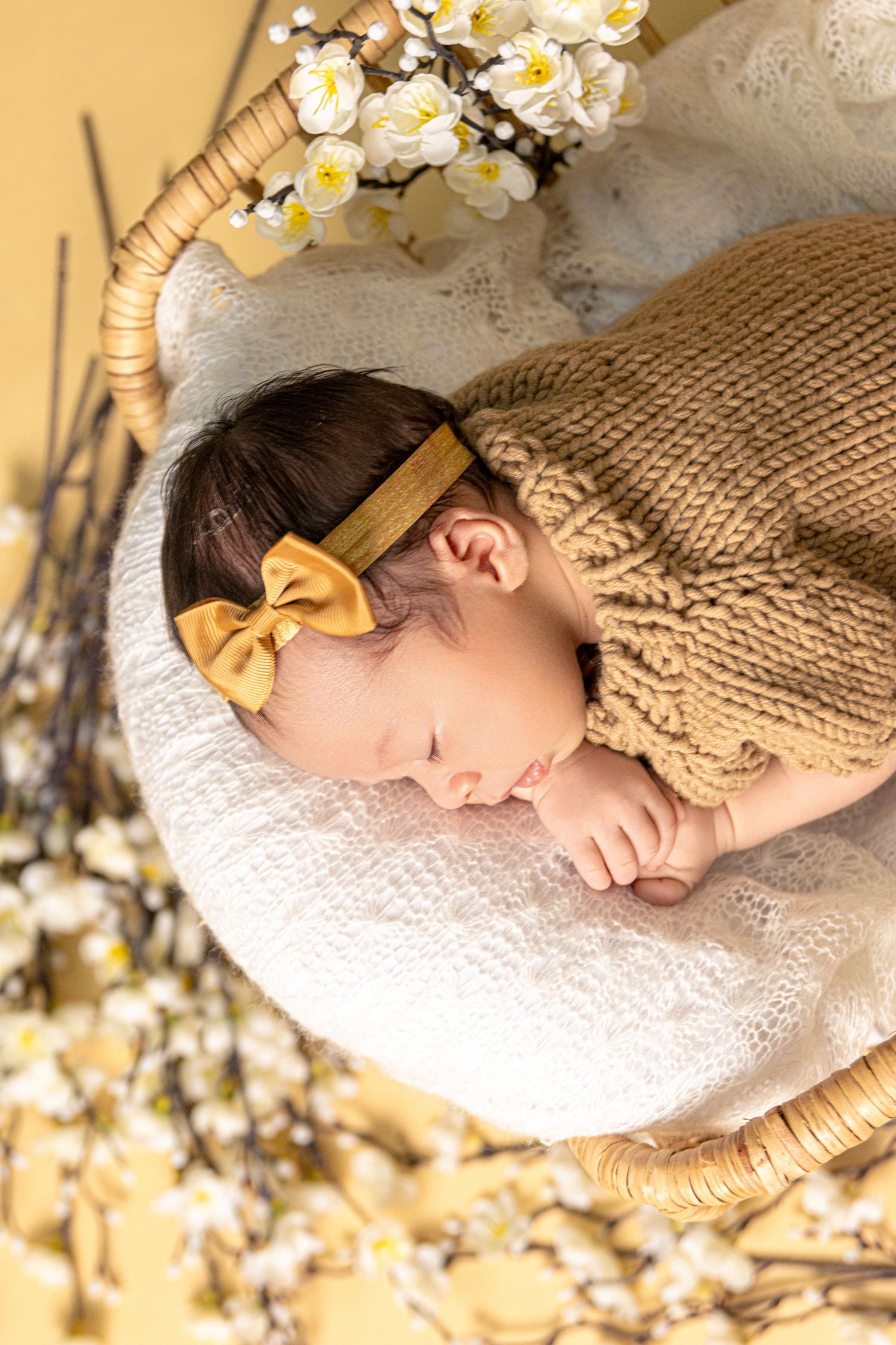 Newborn photography setup with white lace, floral decorations and soft yellow lighting.