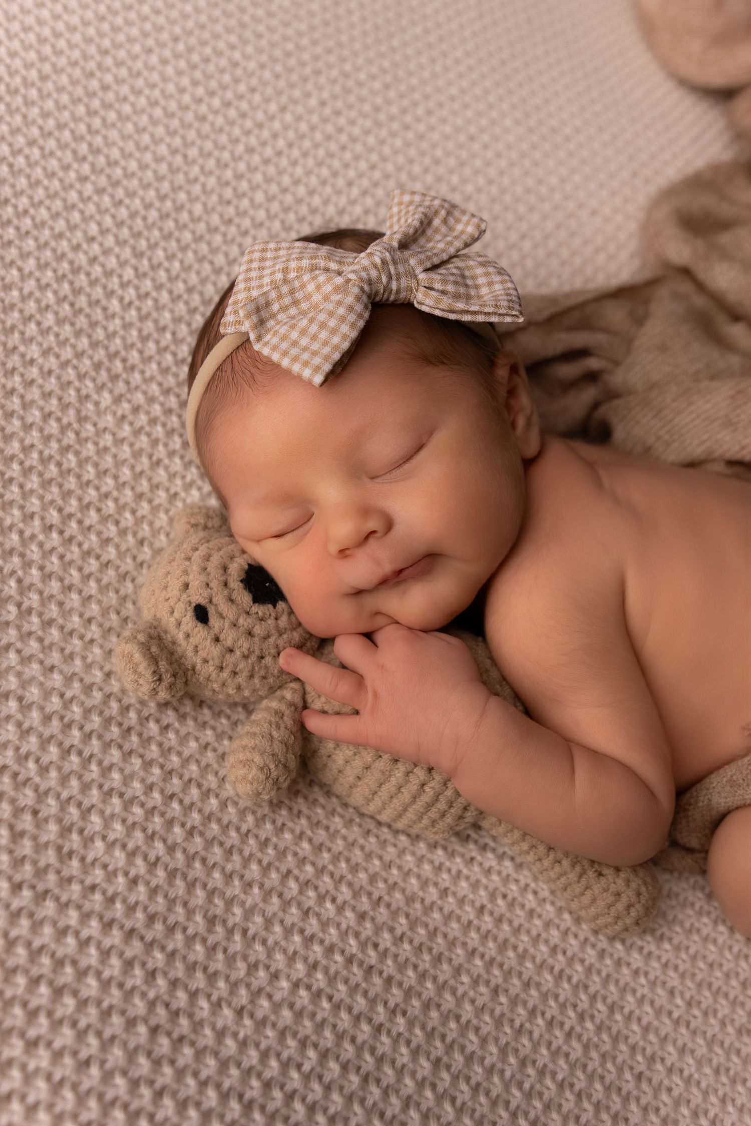 Peaceful newborn portrait with knit accessories and checkered fabric on textured backdrop.