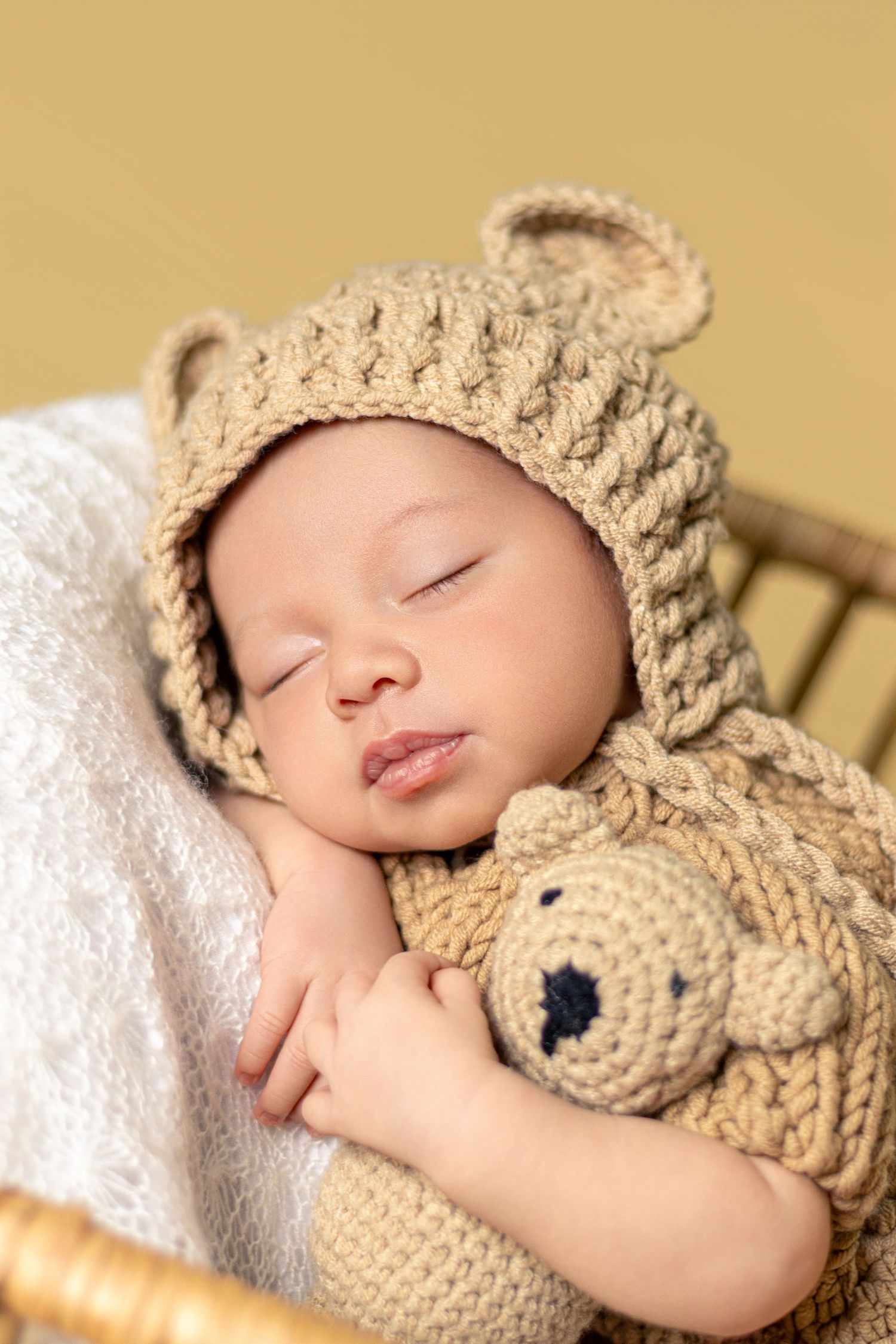 Peaceful sleeping newborn cuddling with beige knitted teddy bear on white blanket.