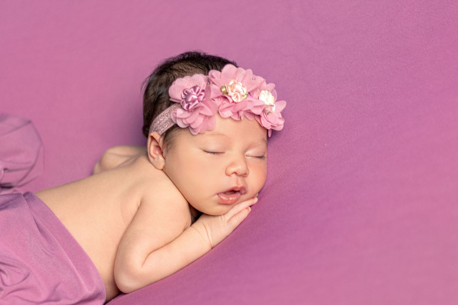 Newborn portrait series on pink background with delicate floral accessories.