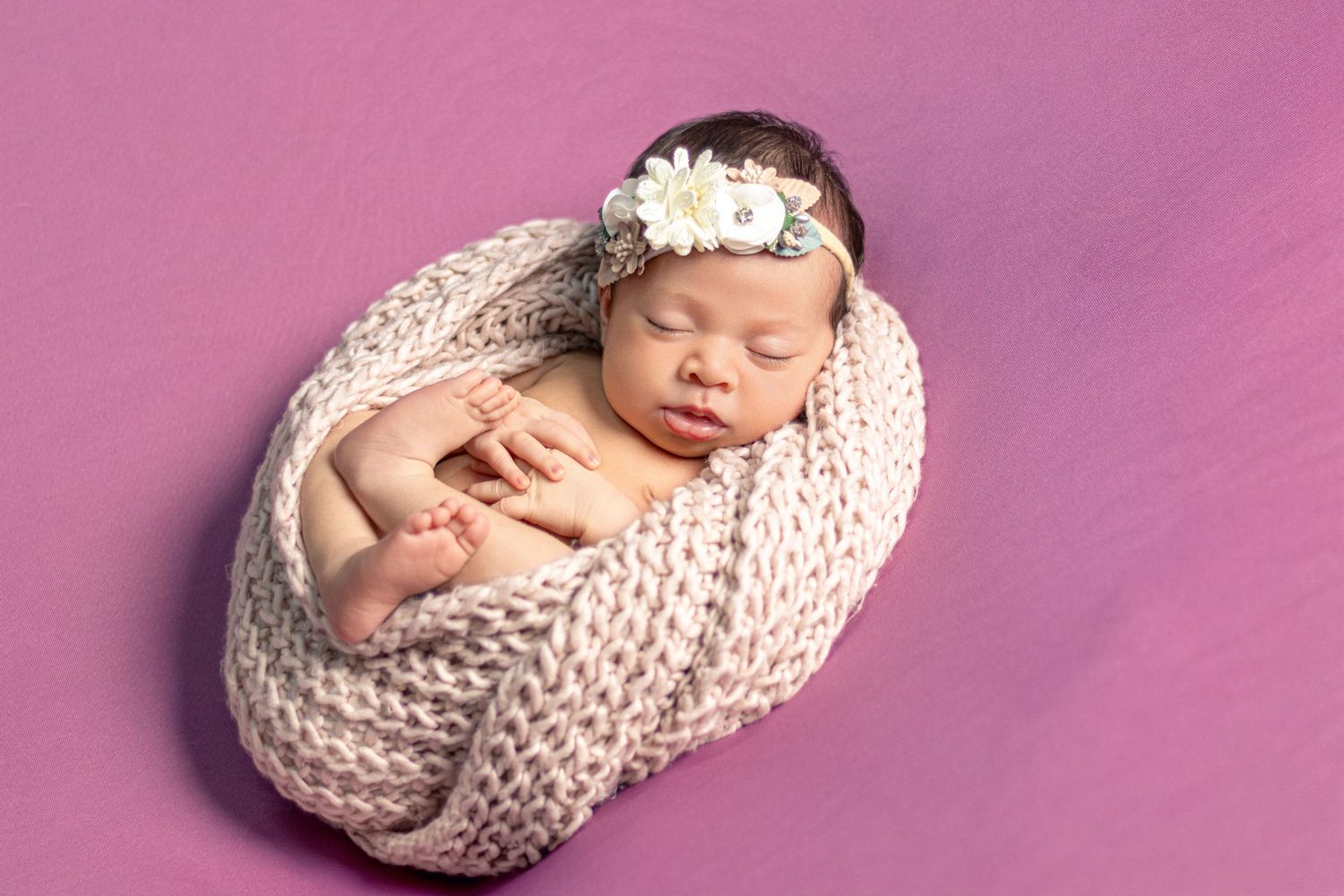 Newborn photography series with baby wrapped in cream knit blanket and white floral headband on pink background.