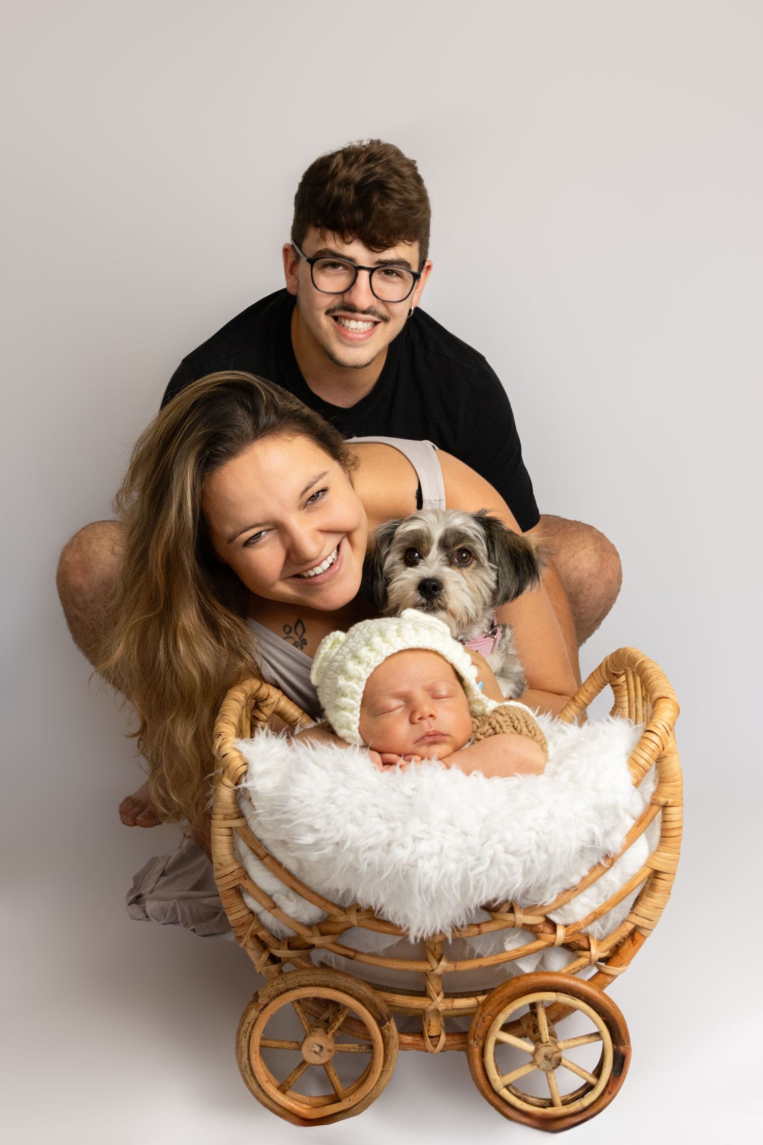 Newborn photography session with a tiny baby nestled in a miniature wicker carriage prop with white fur lining.