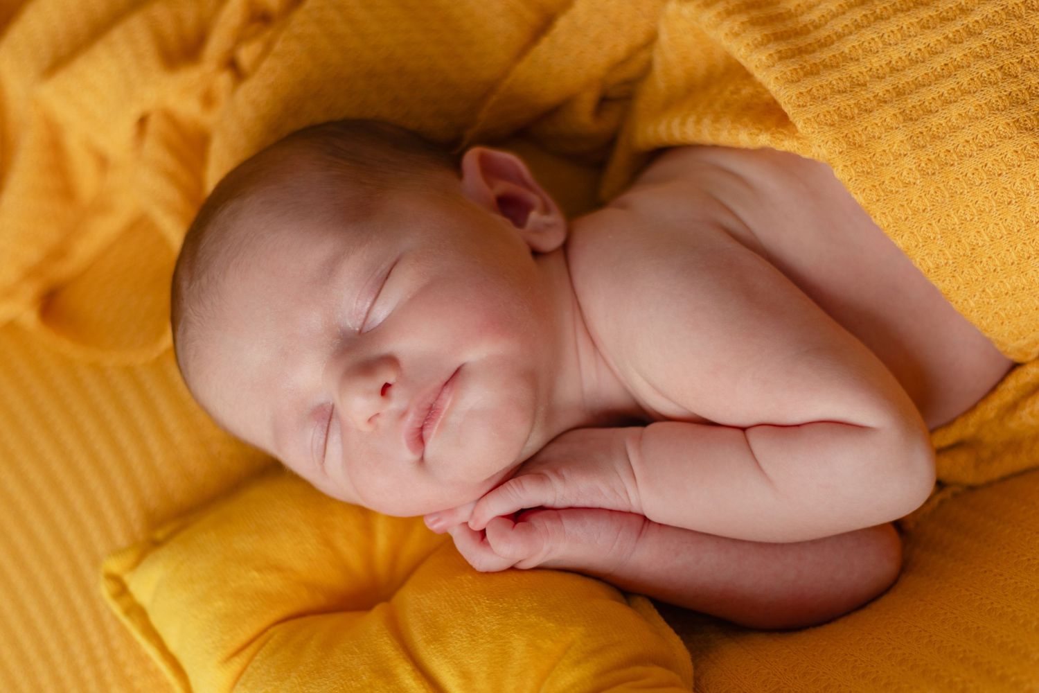Peaceful newborn baby resting on bright yellow quilted background.
