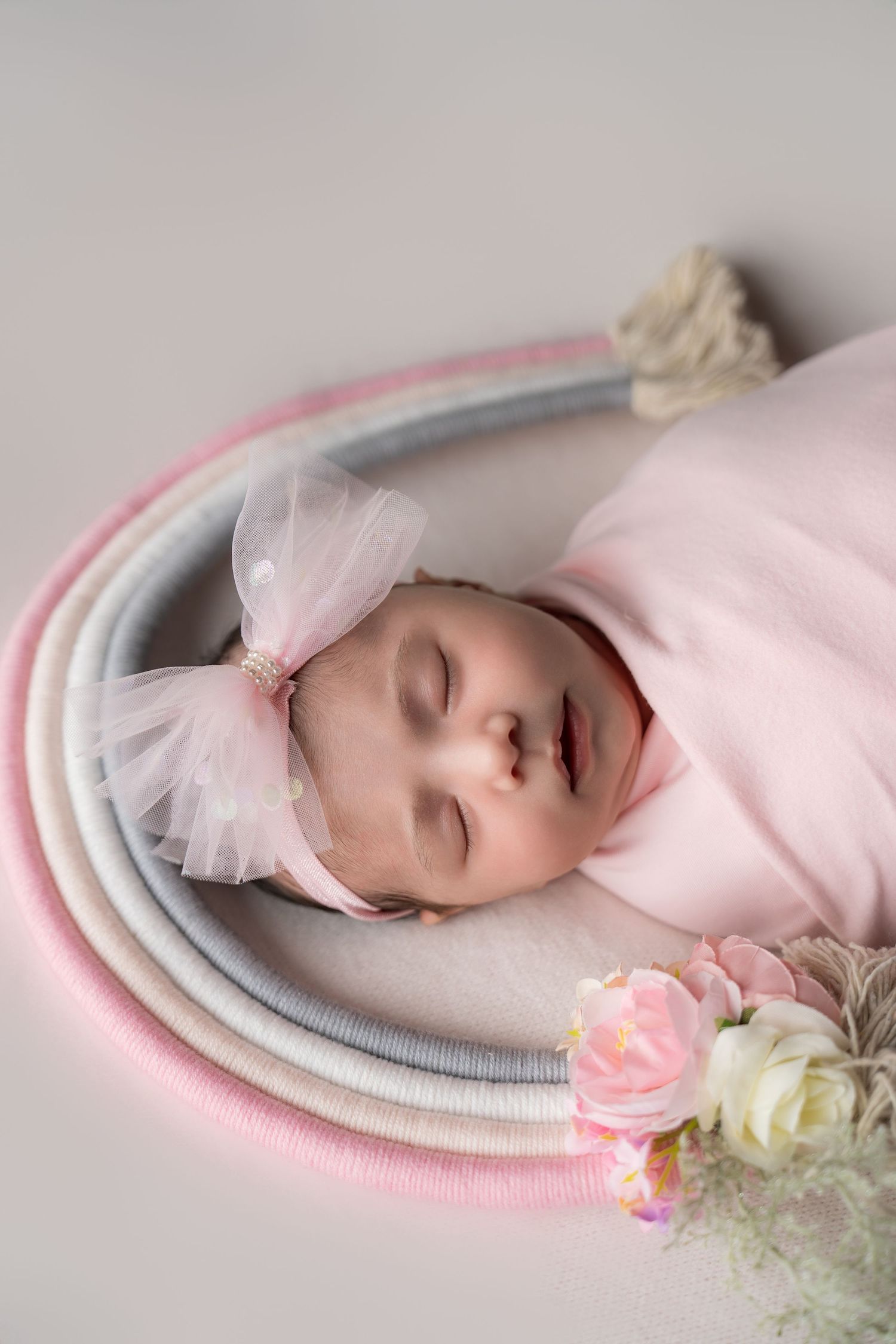 A sleeping baby in pink lies on soft circular blankets with delicate tulle bow and roses as decorative accents.