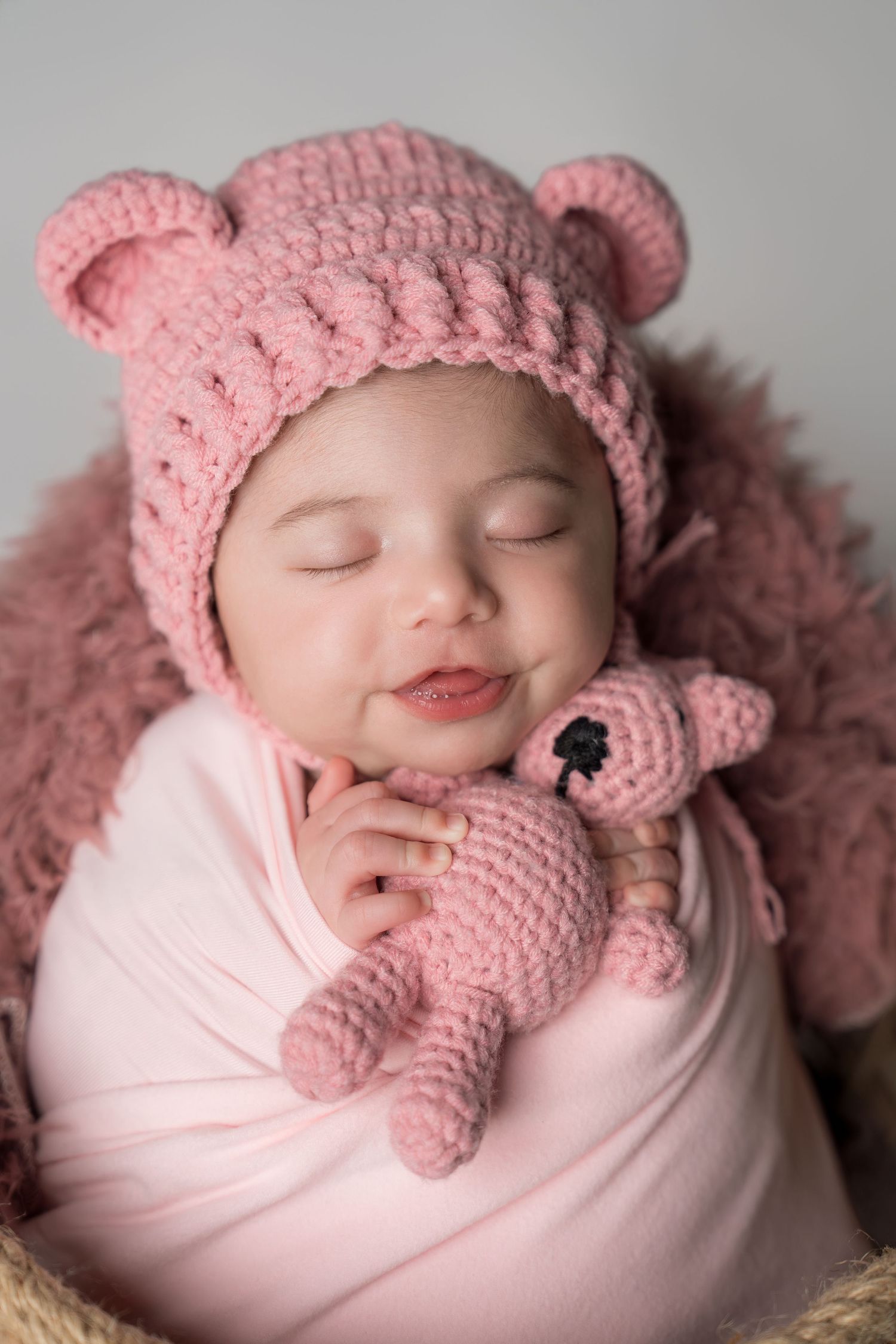 Sleeping newborn wrapped in pink fabric wearing a crocheted pink hat and bear ears.