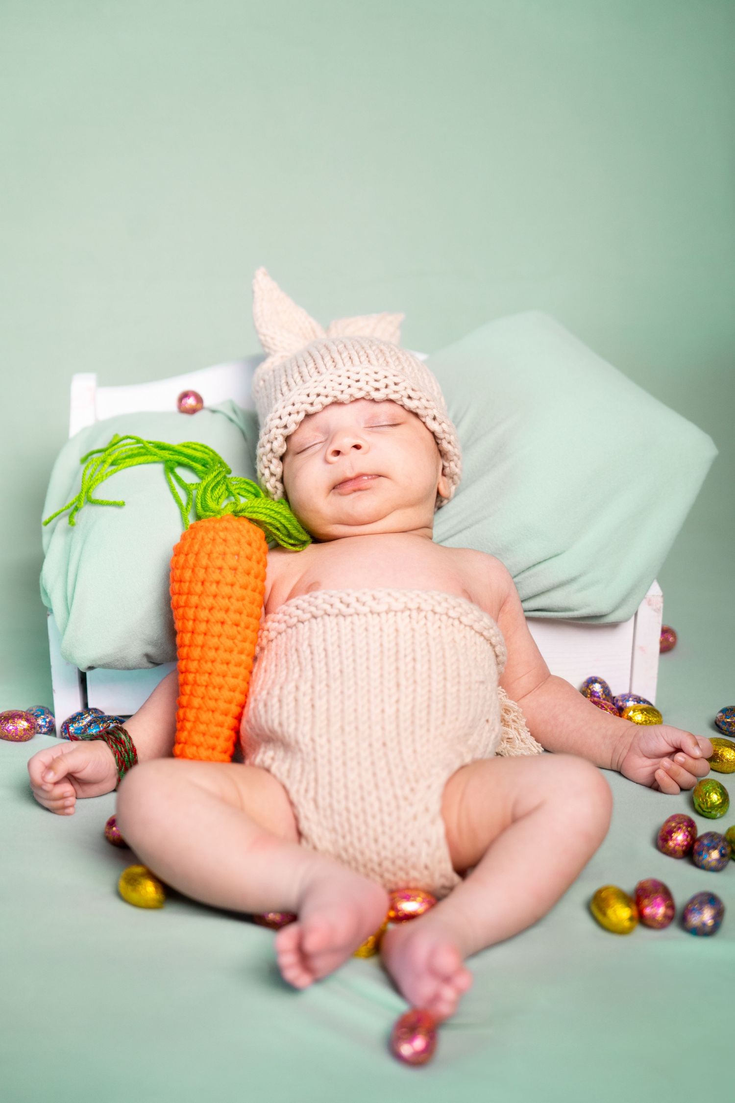 Peaceful sleeping baby in knit bunny costume with carrot prop and Easter decorations.