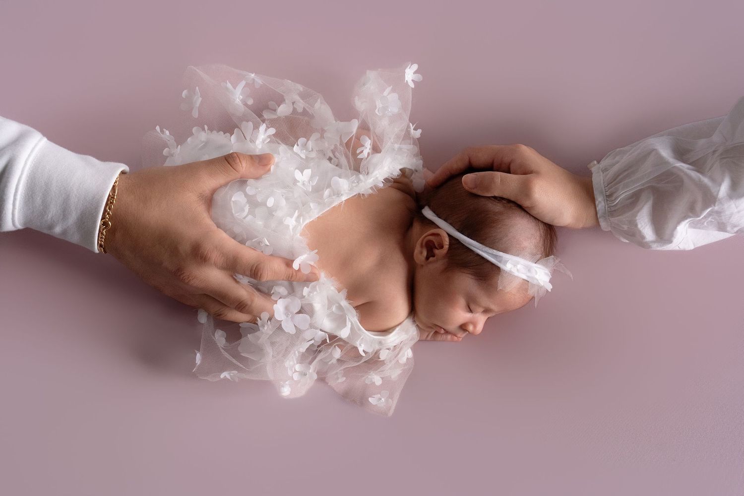 Close-up of baby's hands with delicate white lace accessories on pink background.