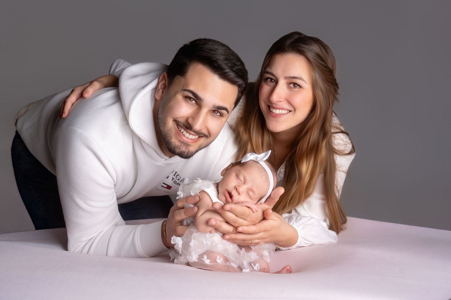 Studio portrait of family with newborn baby on grey background.