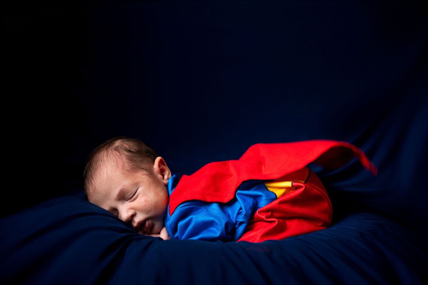A child in red and blue sleepwear rests peacefully against a dark background.
