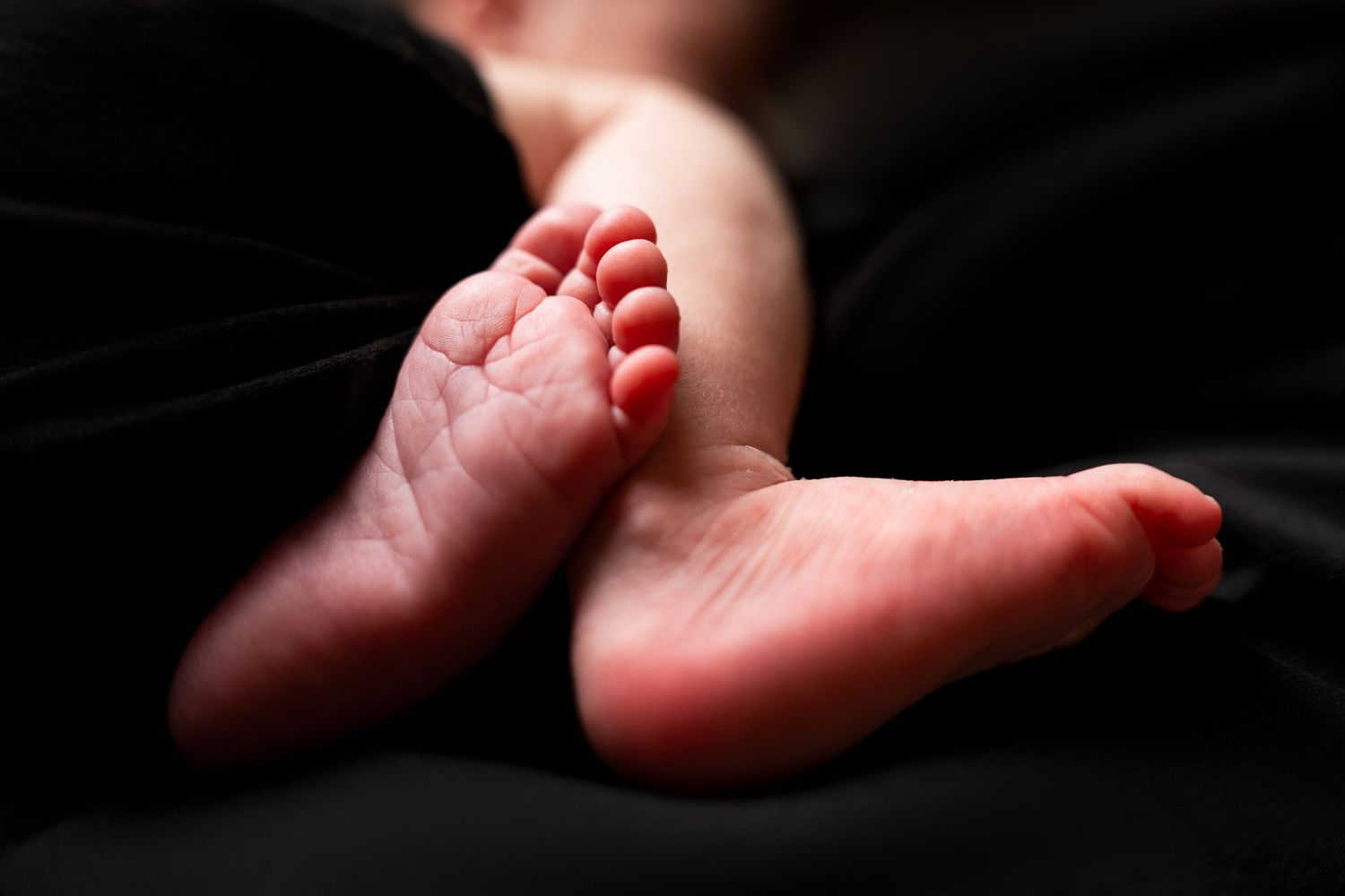 Close-up shots of tiny baby feet illuminated against a dark background.
