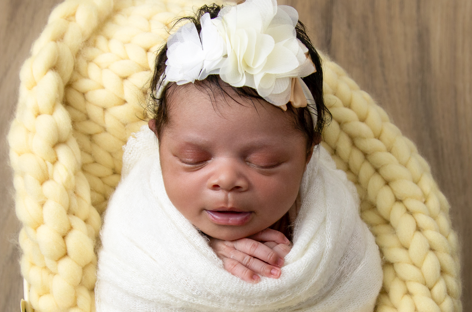 Sleeping newborn wrapped in cream knit blanket with white bow headband.