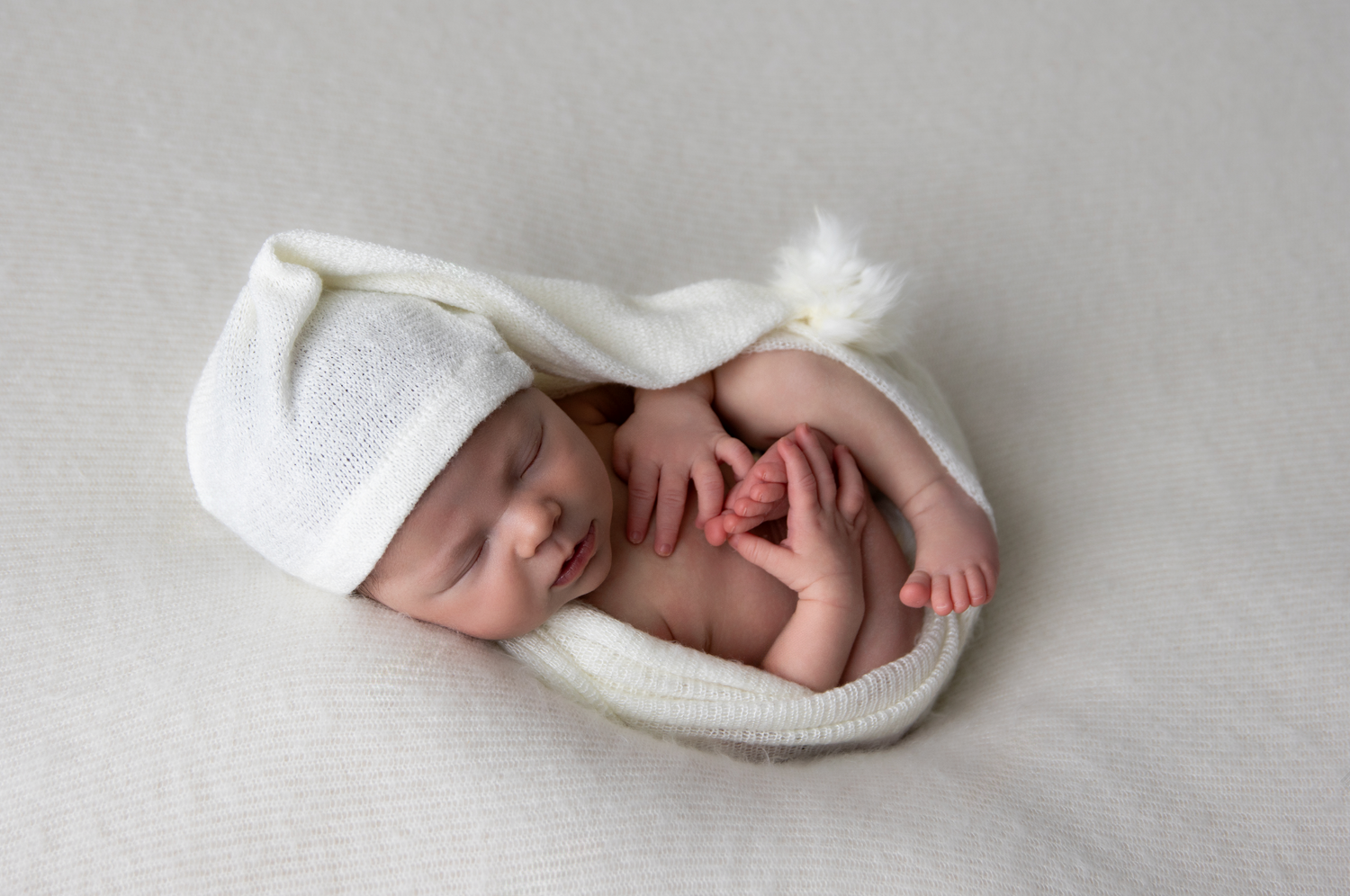 Peaceful newborn wrapped in white fabric against light grey background.