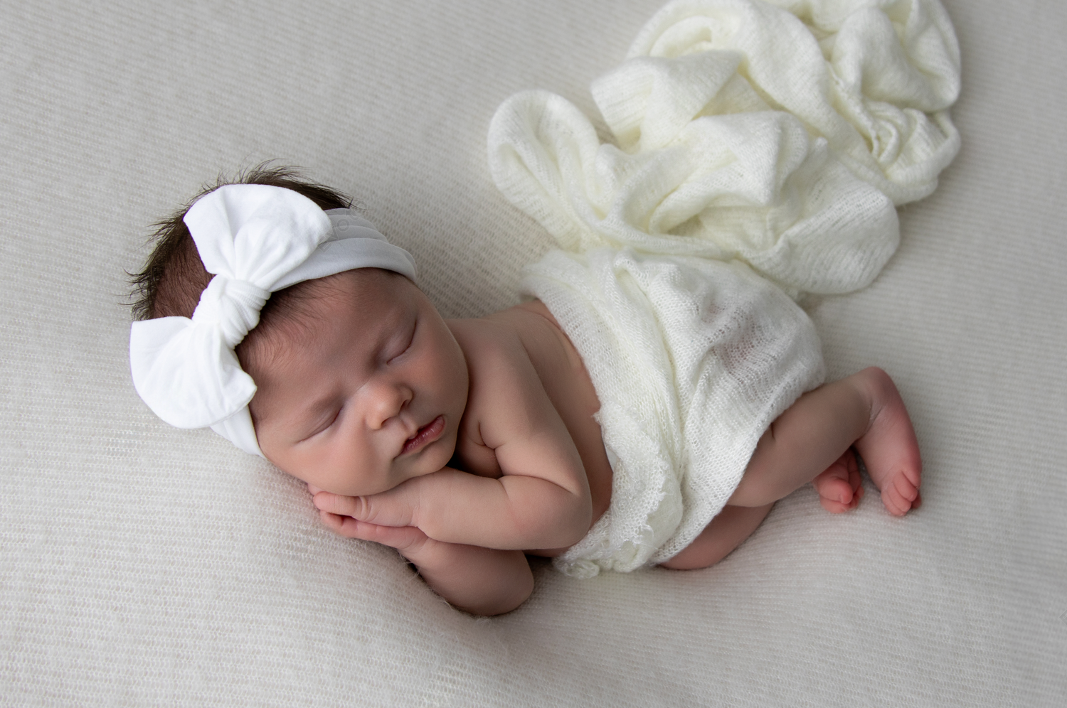 Newborn baby wrapped in soft white fabric sleeping on light grey background.