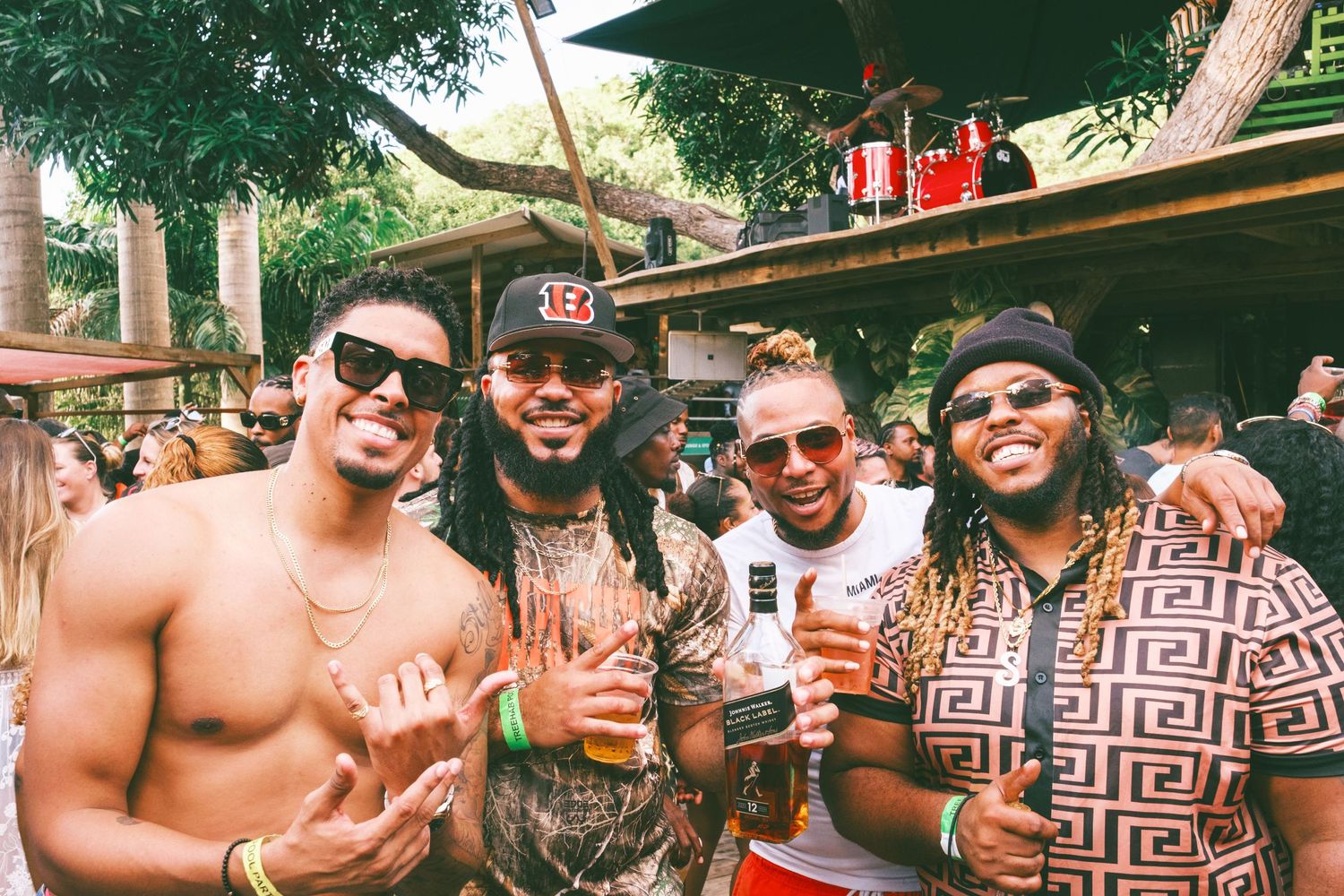A group of friends enjoying drinks together at an outdoor summer party with trees in the background.