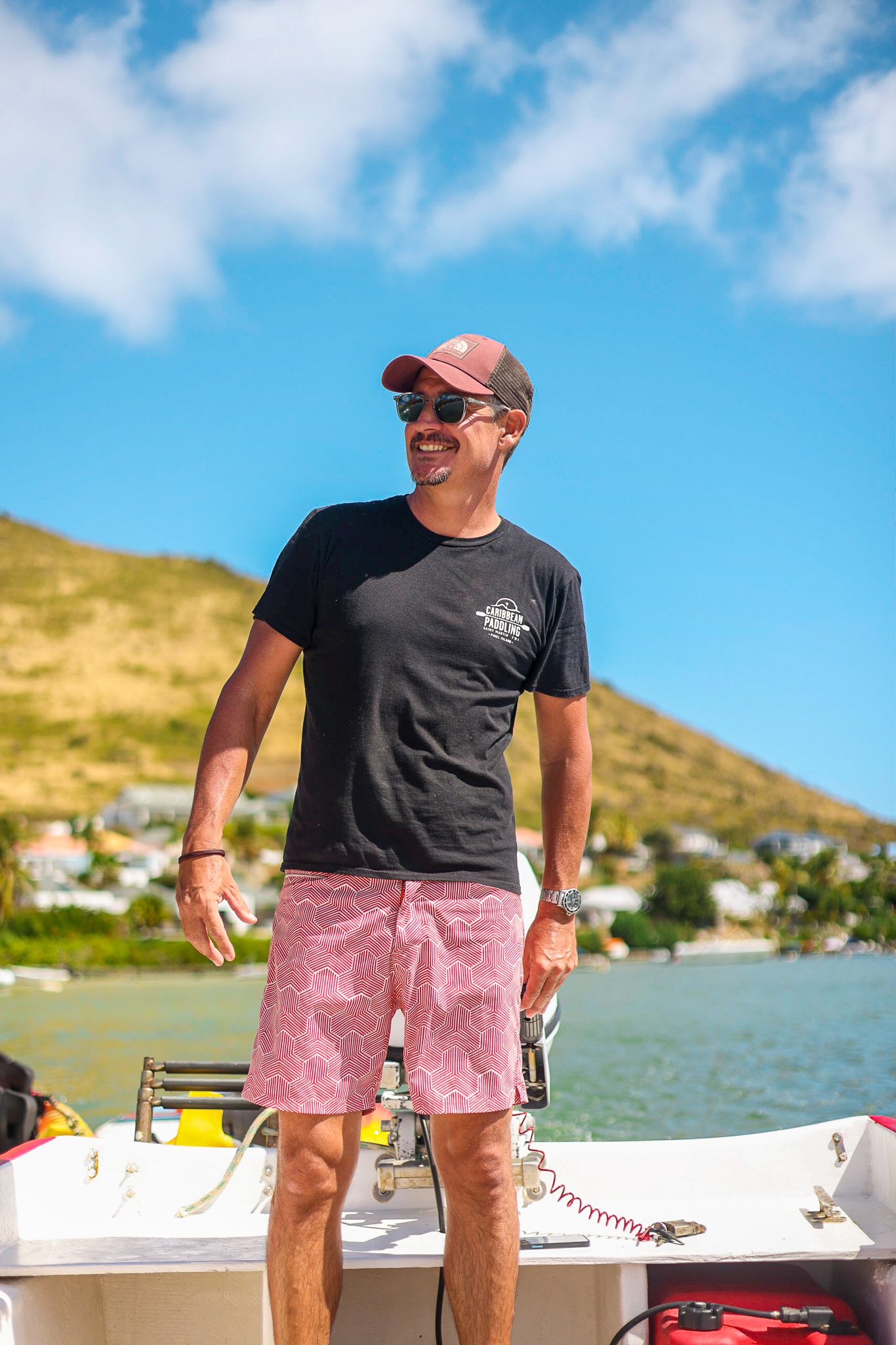Person enjoying a sunny day on a boat wearing pink shorts, black t-shirt and baseball cap against a blue sky backdrop.
