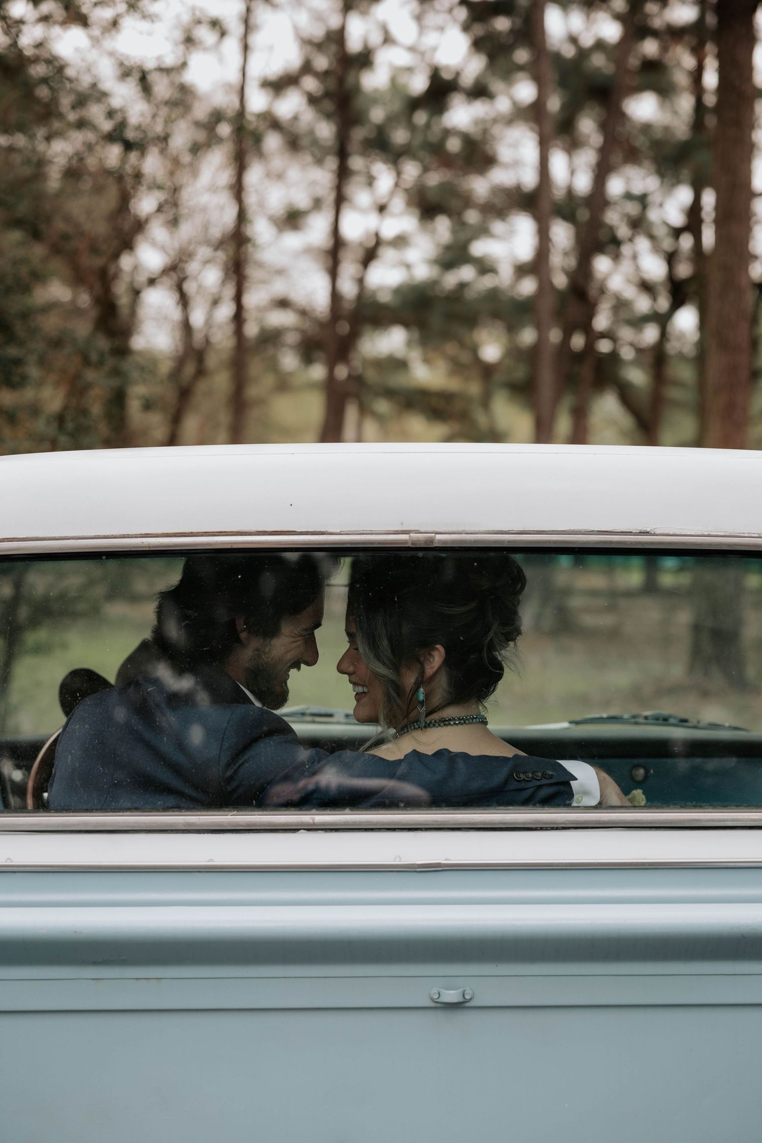 A couple shares an intimate moment seen through a classic car's passenger window.